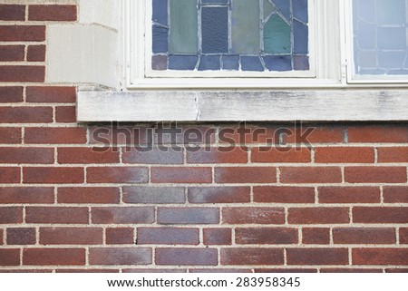 Contractor cleaning issues. Close up of dirty red clay brick building with stained glass window shows white deposits on the brick. Mixed substrates