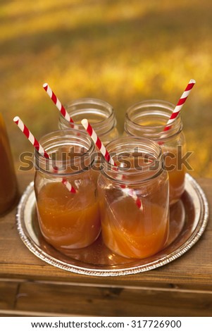Four jars of apple cider with stylish striped straws sit outside. Autumn season. Limited depth of field.