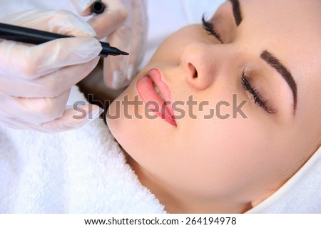 Young beautiful woman having permanent make-up (Tattoo)