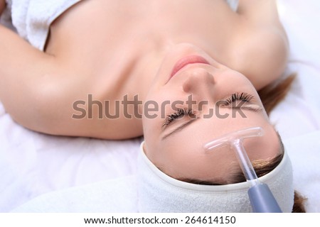 People, beauty, spa, cosmetology and technology concept - close up of beautiful young woman lying with closed eyes having face massage by massager in spa.