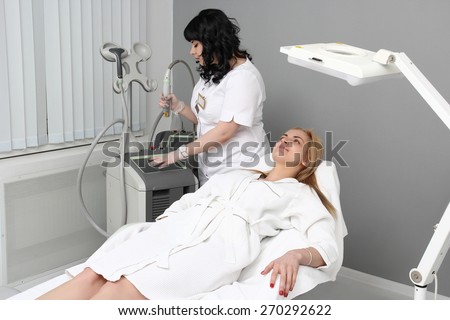 Cosmetologist tuning of the laser for hair removal. The patient lies flat on the couch.