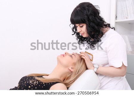Waist-up portrait of a cosmetologist inspecting skin of her patient a young woman with fresh and clean skin seriously looking at her after a professional cosmetology procedures in a beauty salon