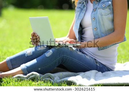 Young business woman working on laptop computer during picnic on green meadows outdoors.