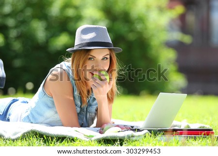 Young business woman working on laptop computer during picnic on green meadows outdoors. Eat green apples.