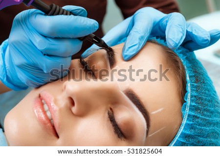 Cosmetologist applying permanent make up on eyebrows- eyebrow tattoo