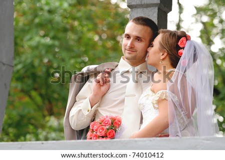 Young couple on a formal wedding photo. The groom kisses his bride while her eyes are closed.