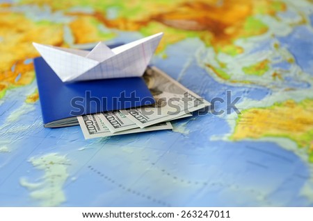 Paper boat, passport, money on a background map of the world. Traveling concept