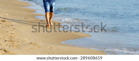 Man walking on sand beach. Closeup detail of man feet and golden sand on beach