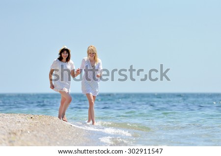 Happy two beautiful womans in white dress running on the beach