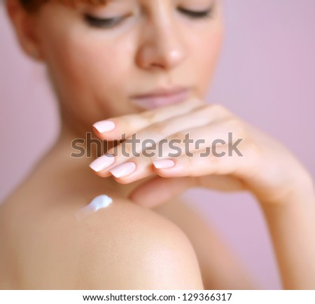 Beautiful young woman with cream on her shoulder. Focus is on a hand