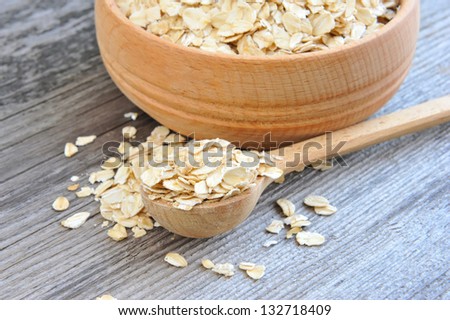 Oat flakes in bowl and wooden spoon on old wooden background