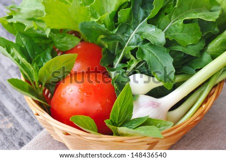 Fresh vegetables and greenery are in a basket on a wooden background