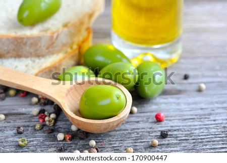 Green olives in a wooden spoon with oil and color peppers on a wooden background