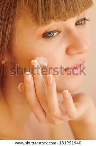 Beauty face of young woman with cosmetic cream on a cheek. Skin care concept
