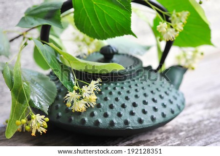 Teapot with linden tea and flowers on old wooden background