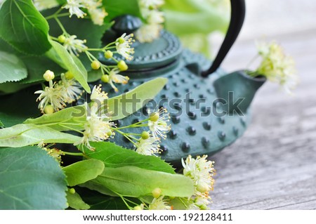 Teapot with linden tea and flowers on old wooden background