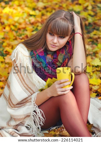 Young beautiful woman that holds the cup of tea in hands on a background autumn leaves