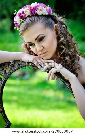 Beautiful young woman in a wreath with vintage mirror outdoors