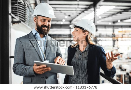 A portrait of an industrial man and woman engineer with tablet in a factory, working.