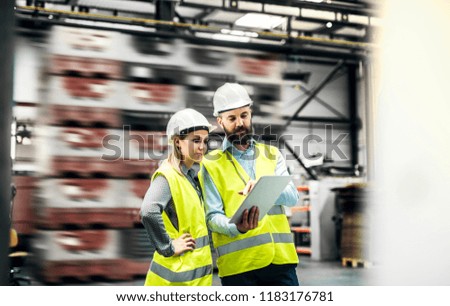 A portrait of an industrial man and woman engineer with tablet in a factory, working.