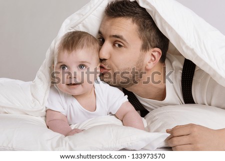 Young father is playing with baby in bed