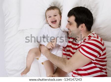 Young father is playing with child in bed