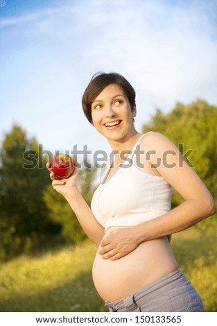 Portrait of young pregnant woman eating apple in nature