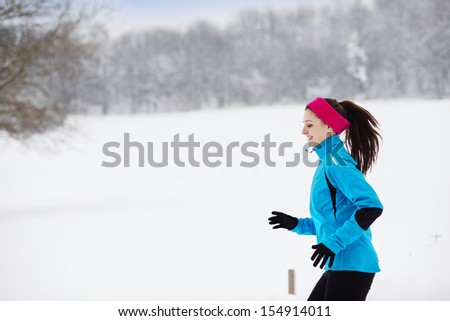 Athlete woman is running during winter in cold snow weather.