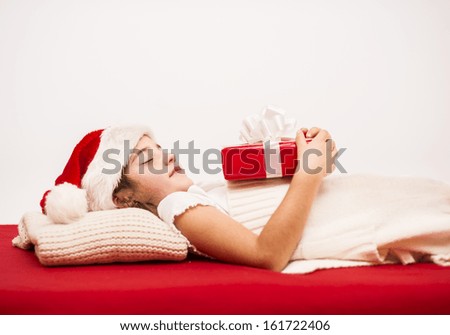Happy small girl in santa hat with christmas gift, lying on the bed