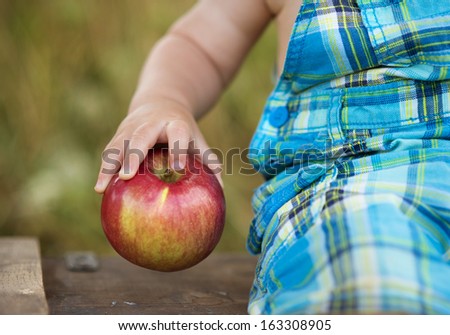 Cute kid holding a red apple in green park