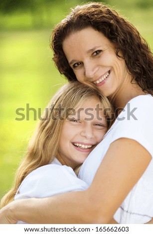 Mother and teenage daughter hugging and smiling together in summer garden.