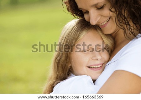 Mother and teenage daughter hugging and smiling together in summer garden.