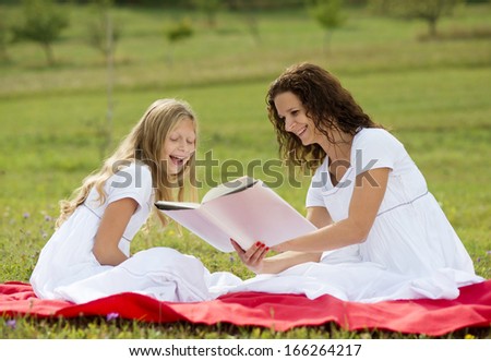 Mother is seating and reading a book to her children in the green park