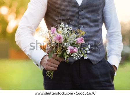 Part of the groom holding wedding bouquet in hand