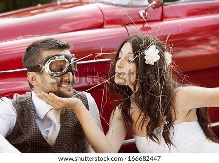 Gorgeous bride and groom having fun with red retro car in nature