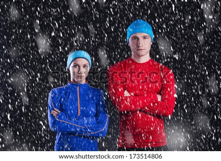 Young fitness athletes are standing outside in cold winter night. Snow is falling around them.