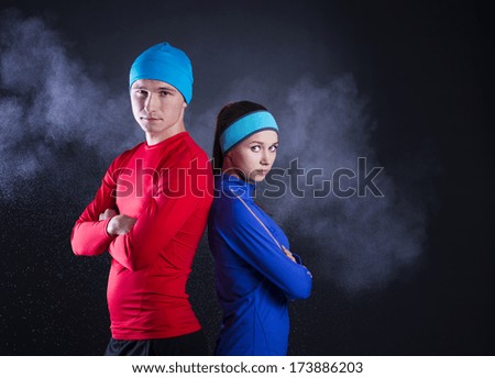 Young fitness athletes are posing in studio with black background. They are dressed in winter sportswear.
