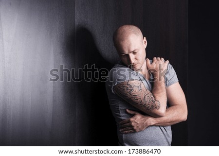 Handsome young man with tattoo is posing in studio with black background and wooden wall