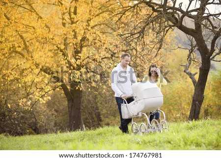 Happy and young family with vintage pram relaxing together in golden and colorful autum nature