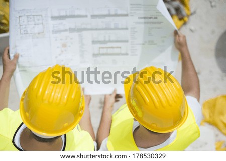 Engineer builders in safety vest with blueprint at construction site