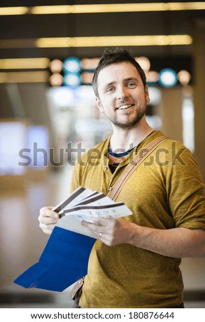 Happy man is checking his air ticket in front of timeboard at the airport.