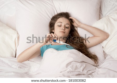 Sick woman with thermometer is lying in bed. She has cold, flu and high fever.