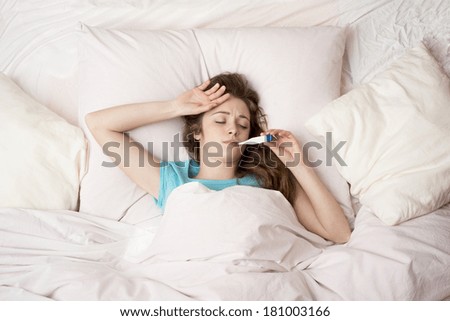 Sick woman with thermometer is lying in bed. She has cold, flu and high fever.