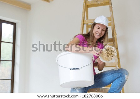 Happy smiling woman painting the walls of new home with paintbrush