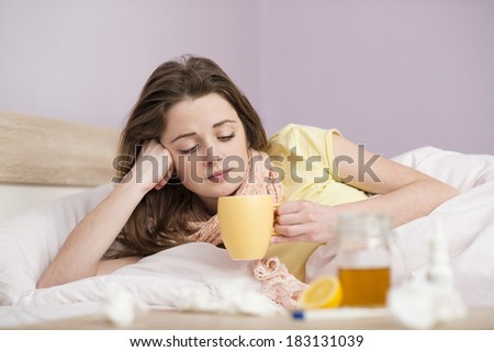Sick woman lying in bed with high fever. She has cold and flu. She is drinking tea with honey and lemon.