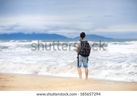 Handsome young Caucasian man walking alone with backpack on the beach