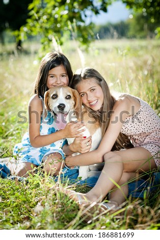 Two sisters playing with their beagle dog in green sunny park