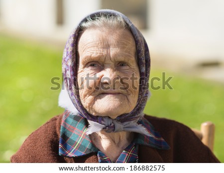 Very old woman with head scarf sitting and relaxing in the garden