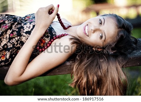 Outdoor portrait of beautiful teenage girl lying down on a bench in green sunny park