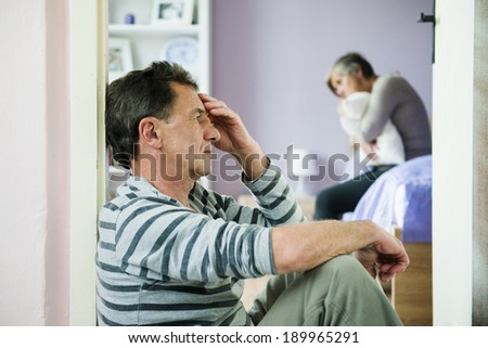 Mature woman siiting on the bed is scared of a man. Woman is victim of domestic violence and abuse.